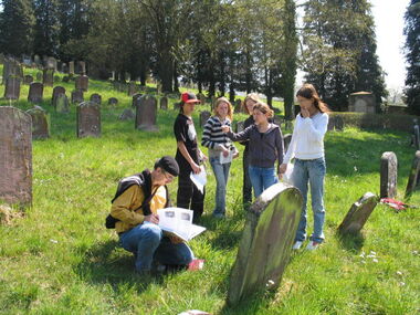 Eine Gruppe von Menschen schauen auf einem jüdischen Friedhof einen Grabstein an